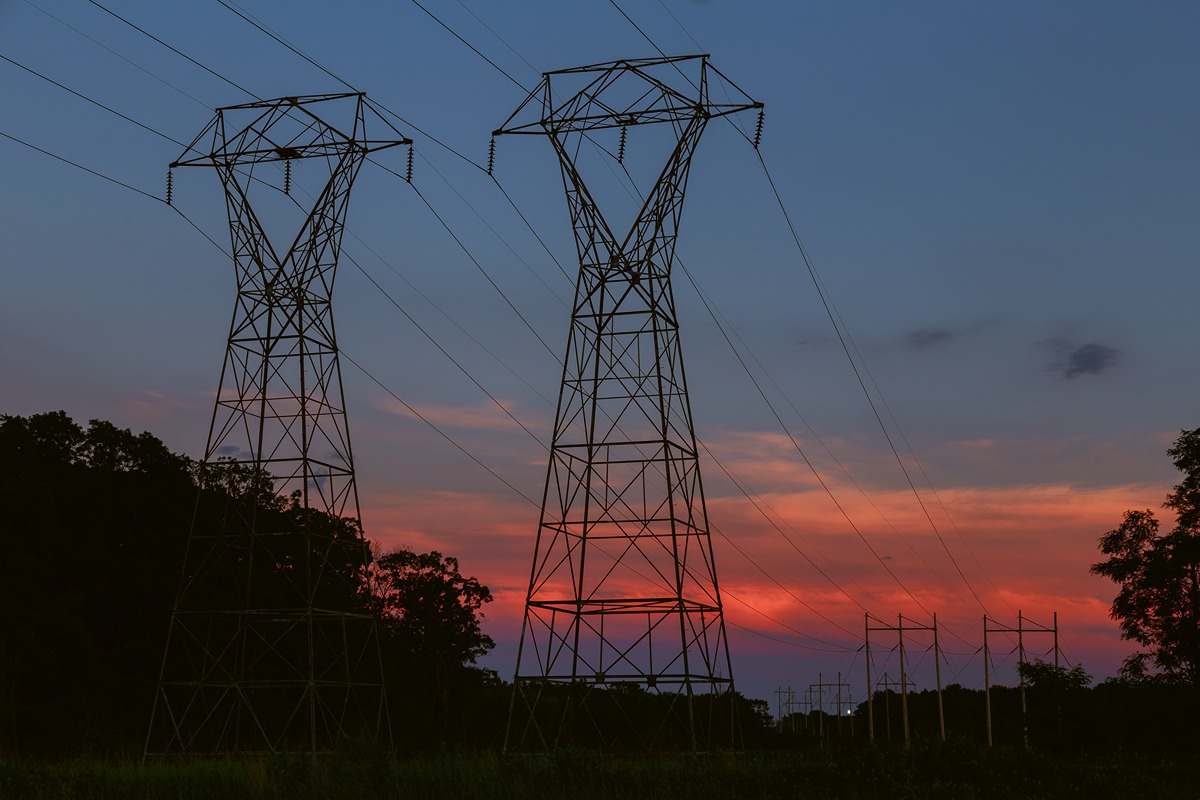 Two large metal electricity pylons with high‑voltage lines against a sunset sky.