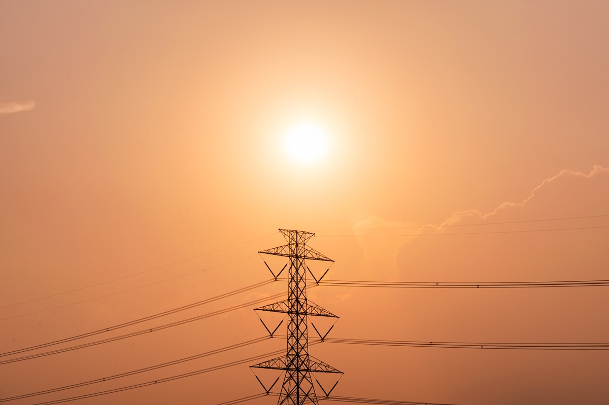 Silhouette of a tall electrical transmission tower with power lines against an orange sunset sky.