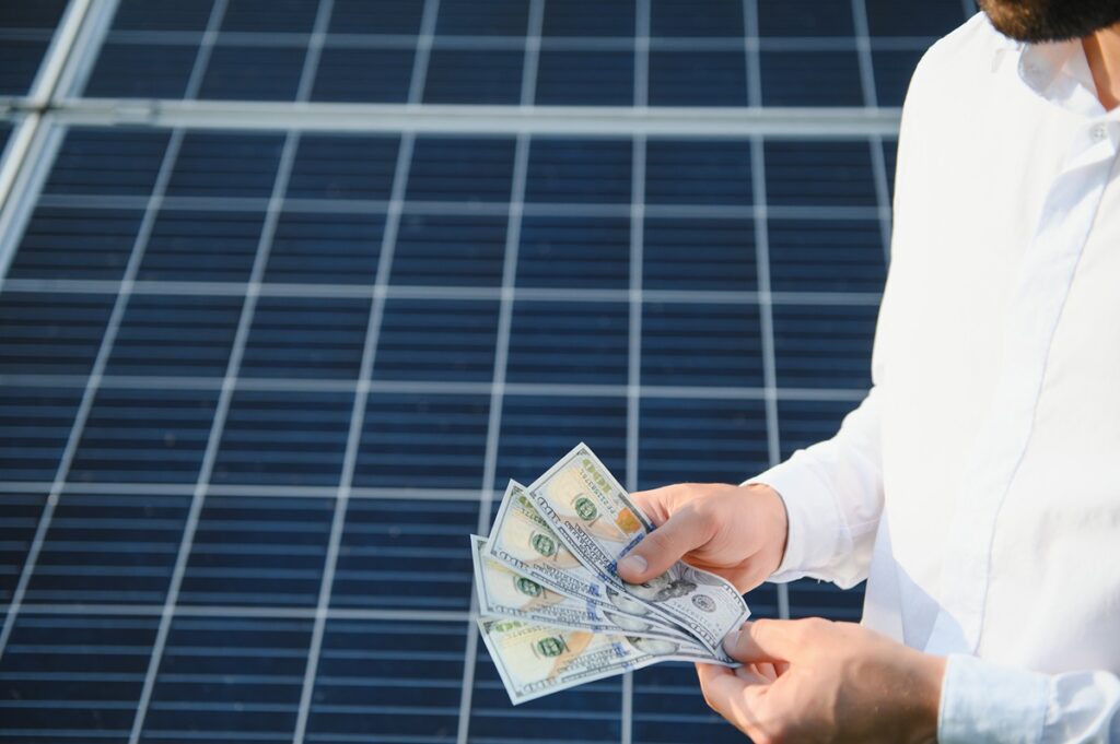 Person in a white shirt counts cash in front of solar panels in the background.
