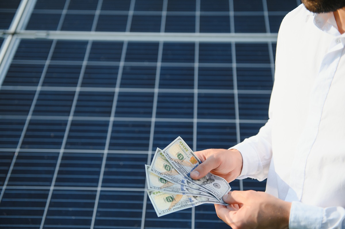Energy Transition Investment Trends Wheres the Money Flowing-Certrec Person in a white shirt counts cash in front of solar panels in the background.