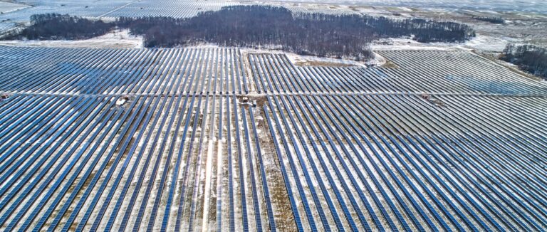 Aerial view of a solar farm with long rows of solar panels in a snowy field.