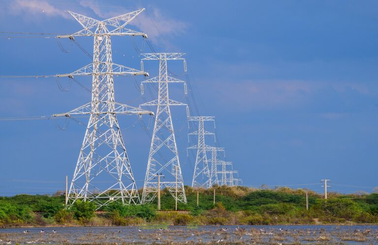New York Imports More Electricity from Canada After High-Voltage Transmission Line Opens-Certrec Row of tall metal electricity transmission towers with power lines stretching across a blue sky over a grassy landscape.