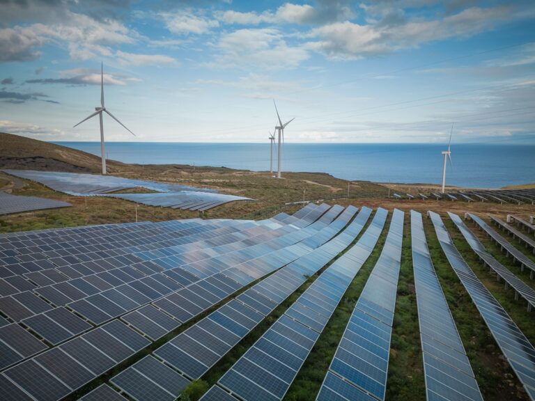 Renewables Deliver 52 of UK Electricity-Certrec Solar panels cover rolling hillside with wind turbines by the ocean in the distance.