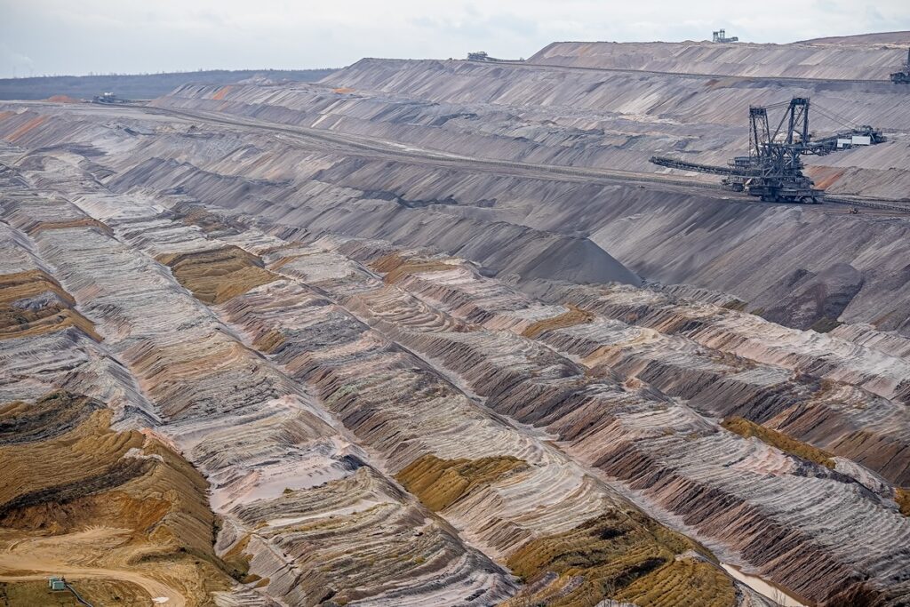 Wide view of an open-pit mine with terraced benches and a large excavator on a conveyor at the top.