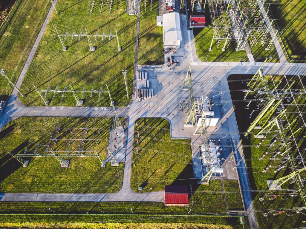 Top down aerial view right above electrical power substation in the countryside Aerial view of an electrical substation with transformers, power towers, and a network of cables across grassy fields and paved roads.