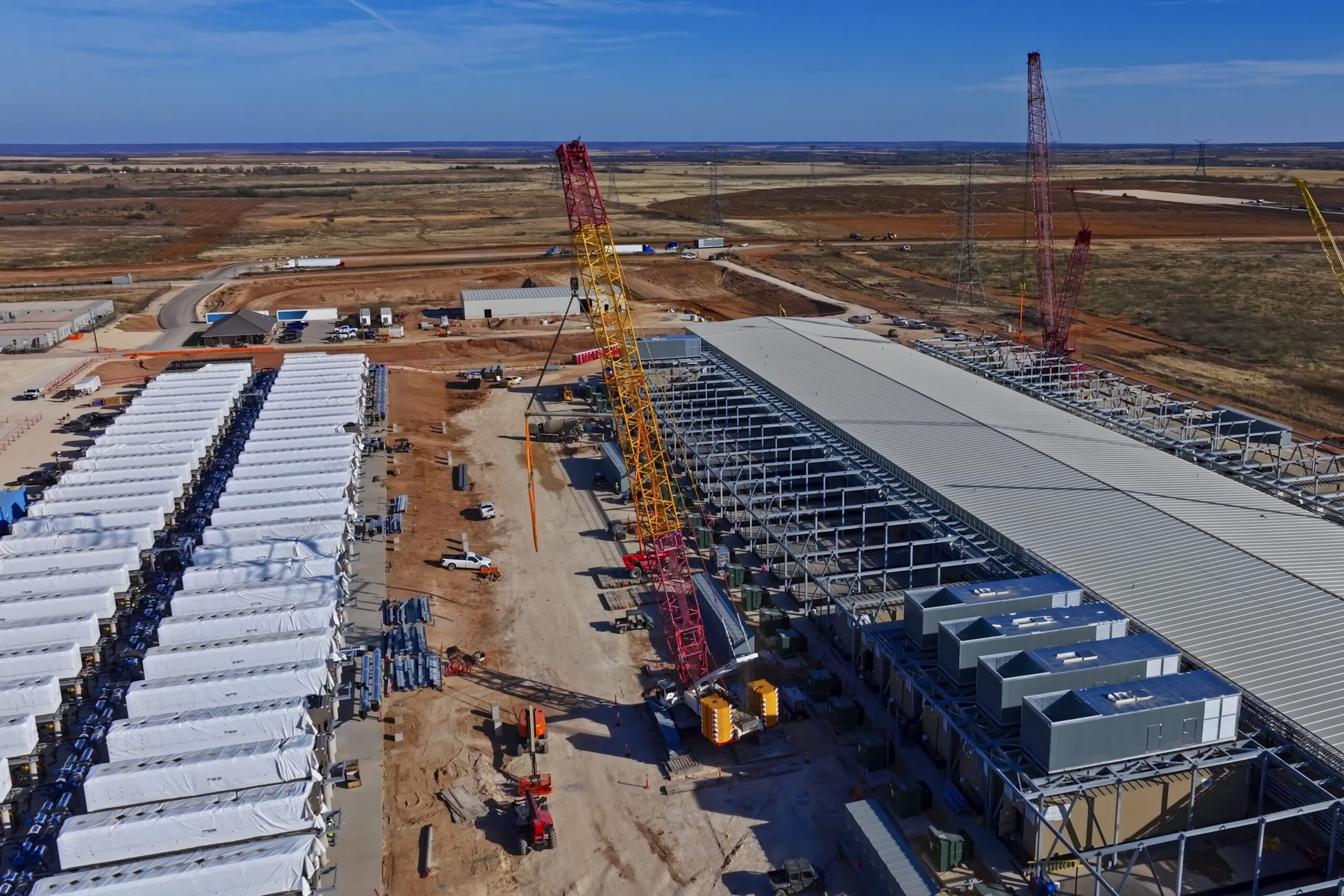 Aerial View of Data Center Construction with BESS Batteries Storage Aerial view of a large industrial construction site with cranes, a partially framed building, and desert landscape beyond.